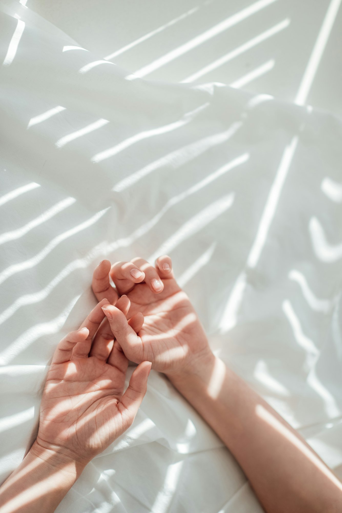 cropped shot of female hands on white bed sheet